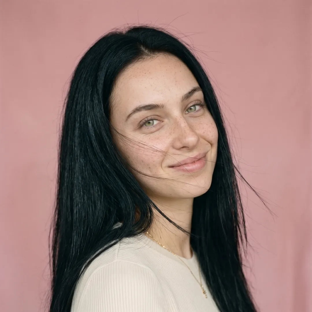 Portrait d'une jeune femme brune souriante avec de longs cheveux lisses et brillants flottant légèrement dans le vent.